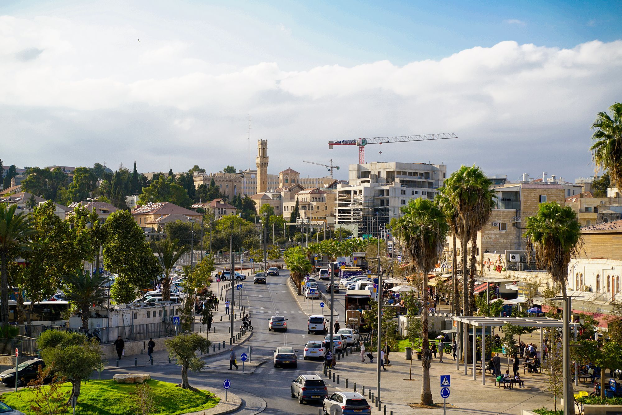 רחוב במרכז ירושלים עם בתי אבן, דקלים ומגדל שעון ביום שמשי